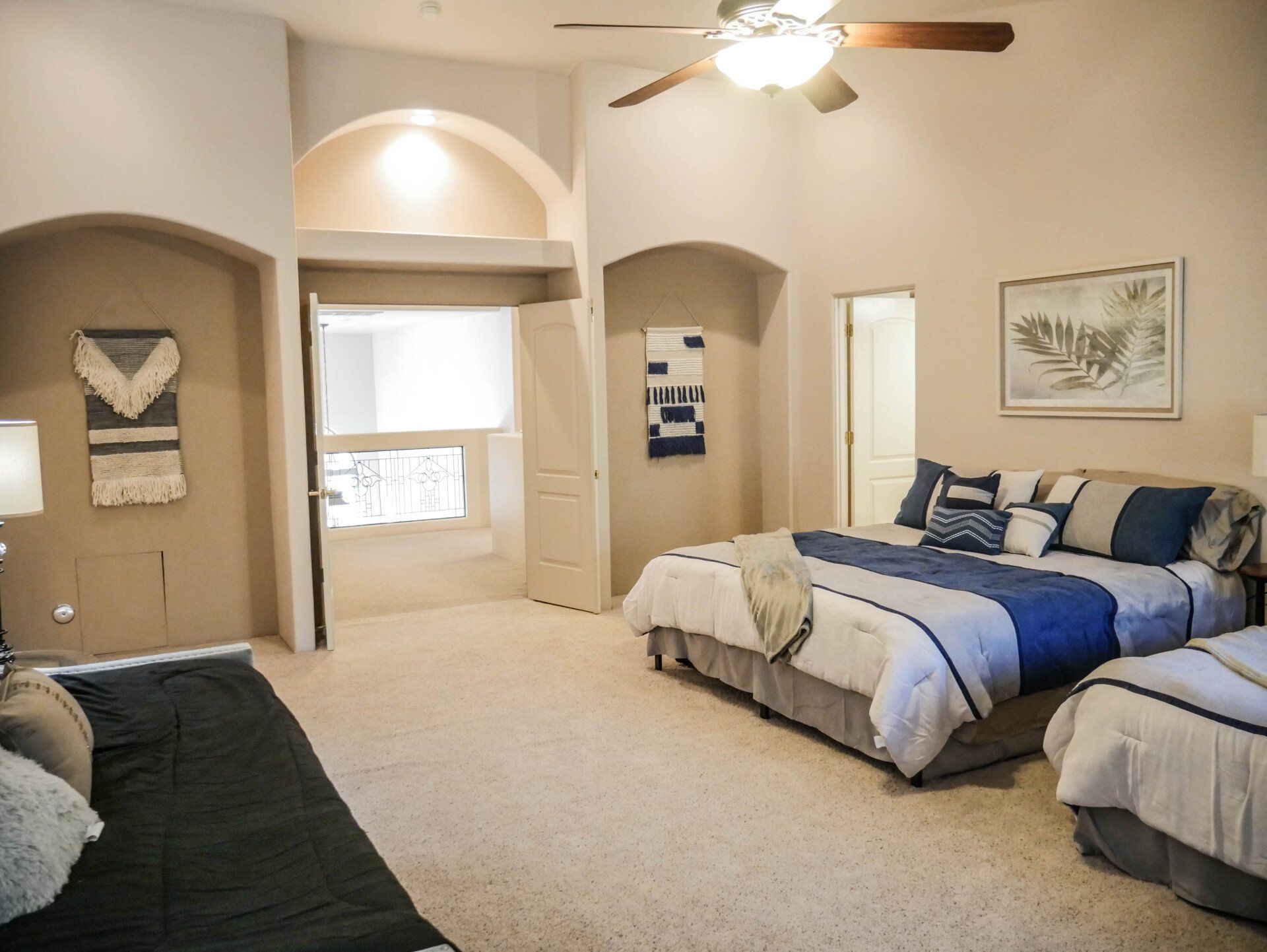 Bright bedroom with beige walls, king bed, twin beds, and a ceiling fan