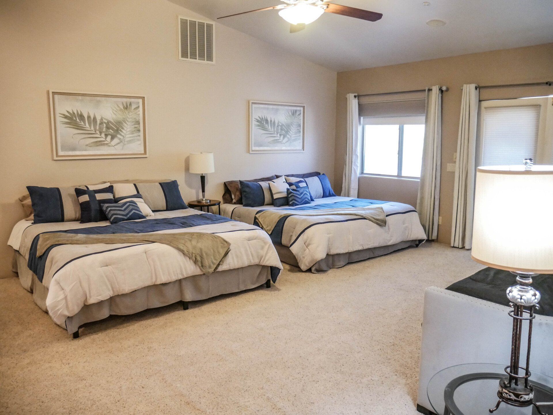 Spacious bedroom with two twin beds, beige carpet, ceiling fan, and a bright window seat.
