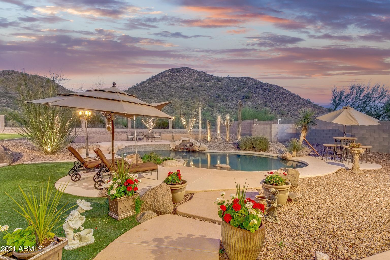 Desert resort pool at sunset with loungers, umbrellas, potted flowers, and mountain views