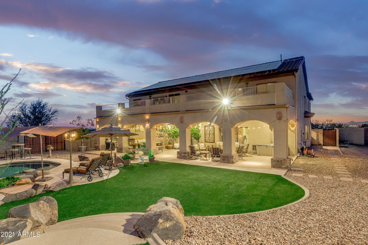 Luxury house with arched patio, green lawn, gravel yard, and sunset sky