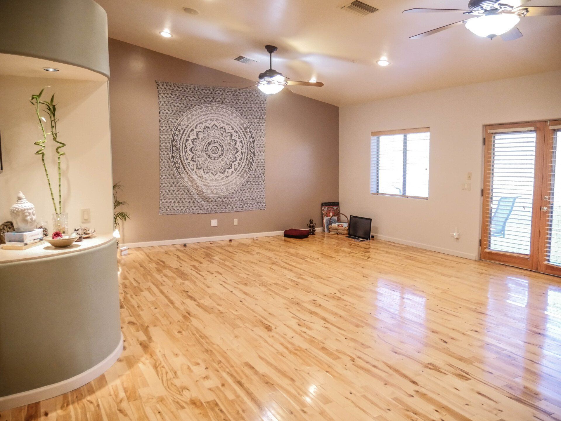 Spacious empty living room with wood floors, ceiling fans, wall tapestry, and sliding glass door.