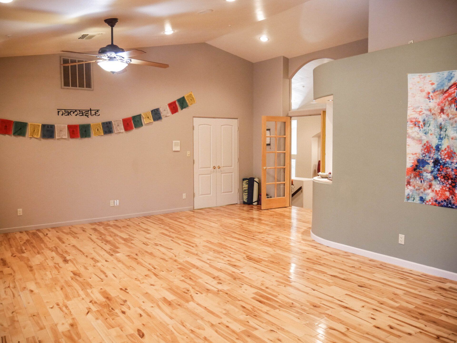 Empty room with hardwood floors, beige walls, ceiling fan, and colorful prayer flags along one wall