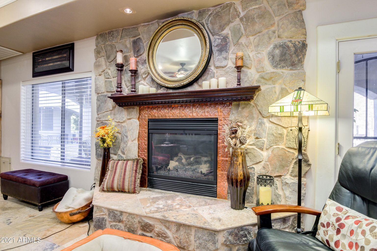A living room with a fireplace , chair , lamp and mirror.