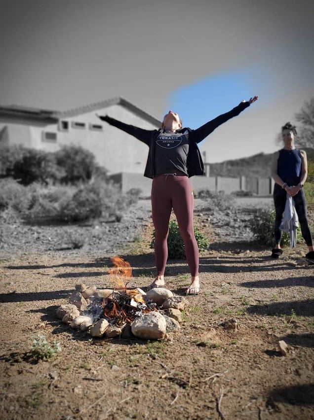 A woman is standing in front of a fire with her arms outstretched.