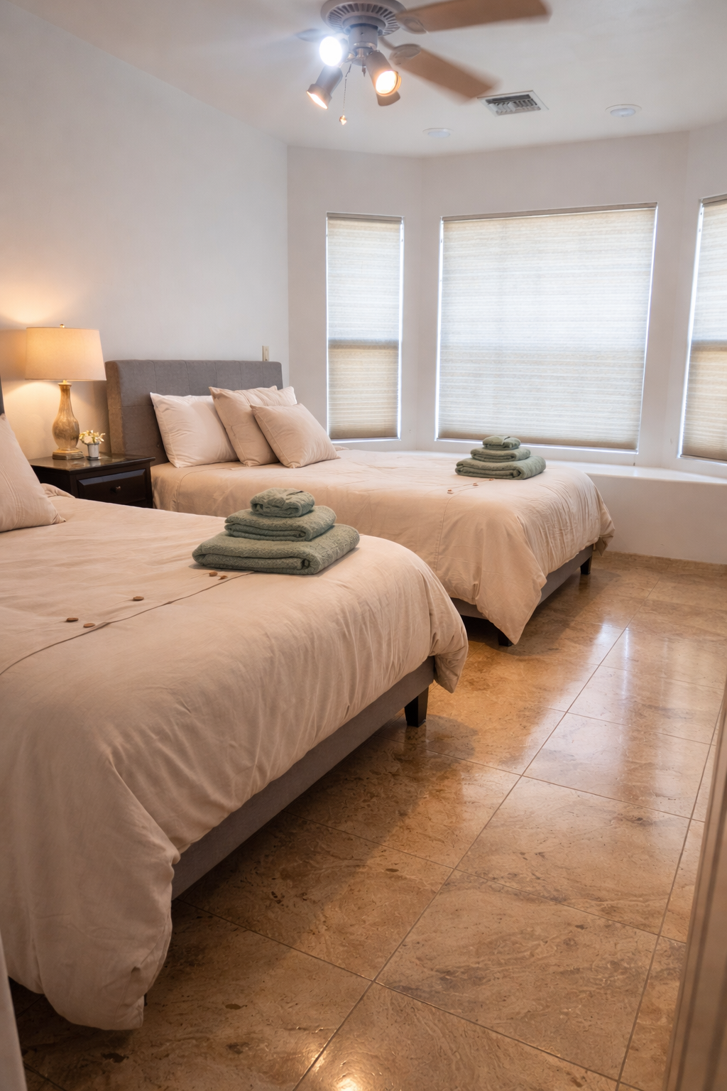 Bright bedroom with two beige beds, a window seat, and soft neutral decor