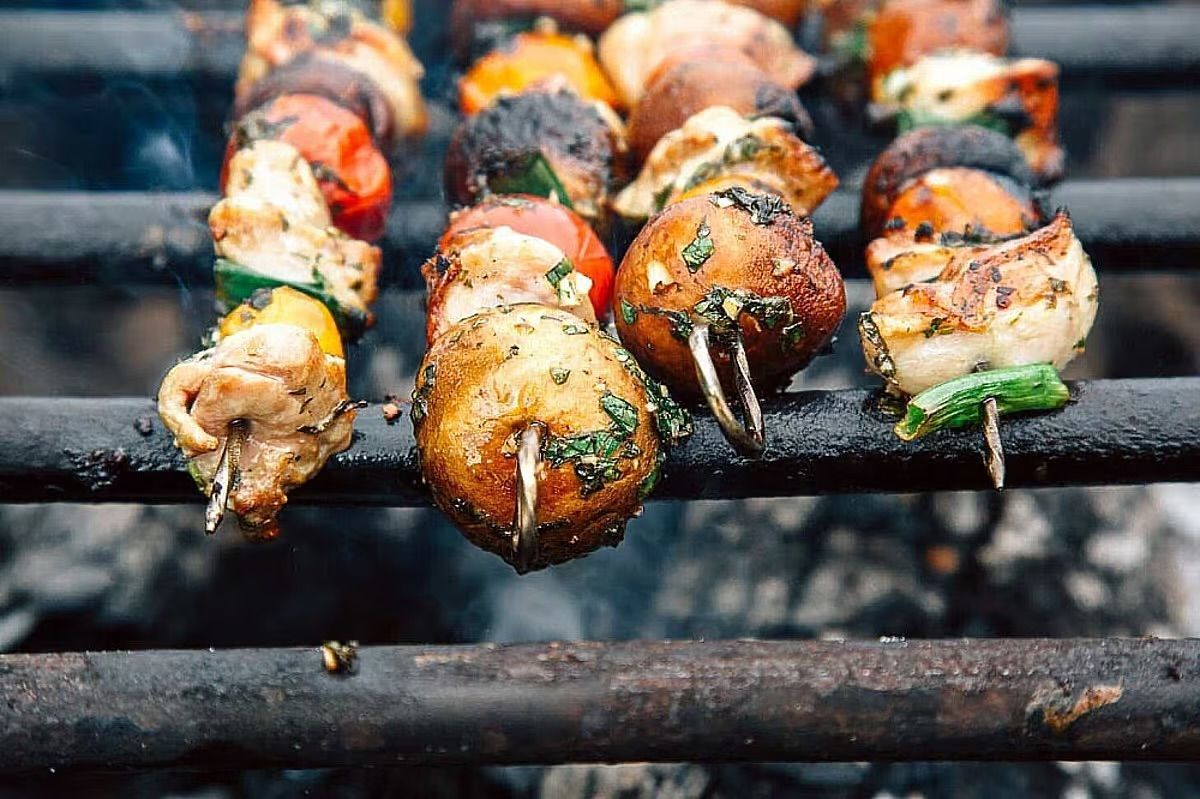 Skewers of grilled vegetables and meat sizzling over a charcoal grill