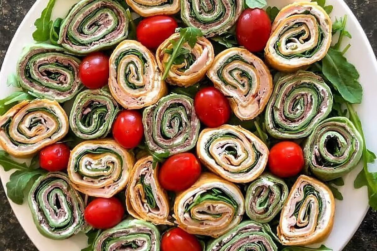 Plate of rolled pinwheel sandwiches with greens and cherry tomatoes
