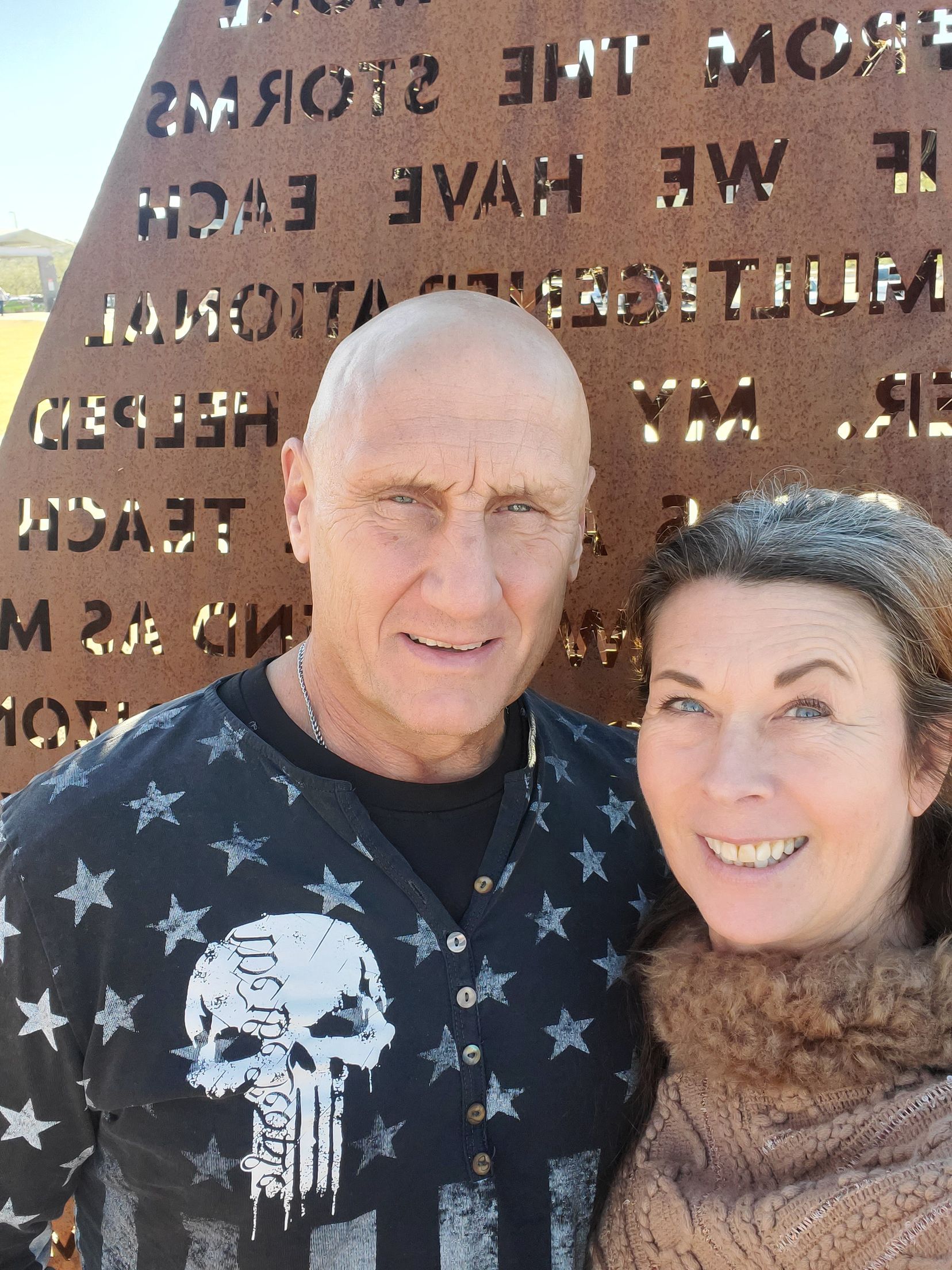 Two people smiling in front of a memorial plaque outdoors