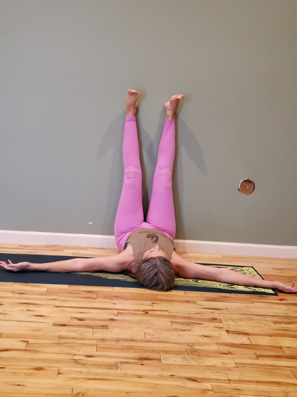 Person doing a legs-up-the-wall stretch on a wooden floor against a gray wall