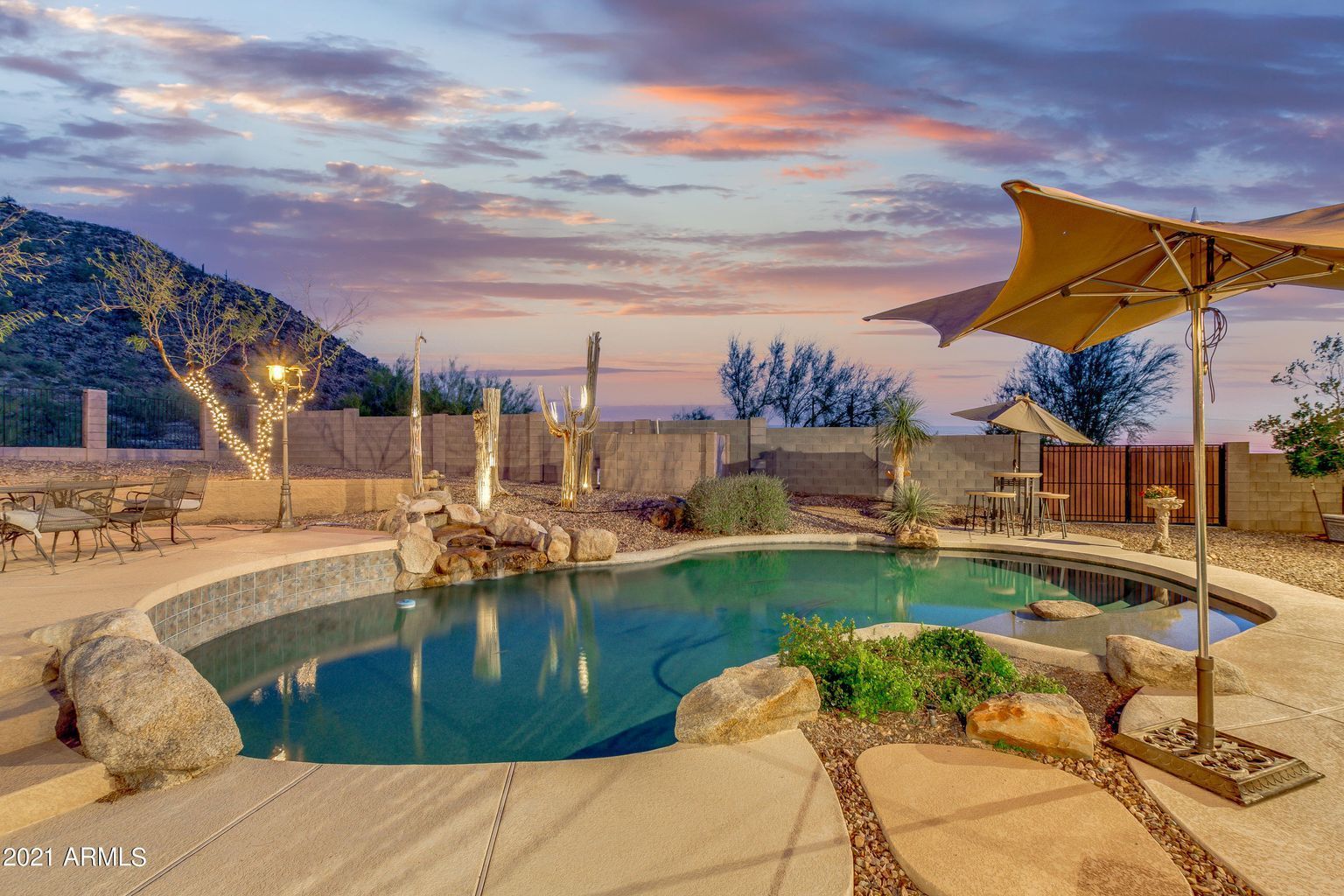 Backyard pool at sunset with desert landscaping, rock waterfall, and patio umbrella