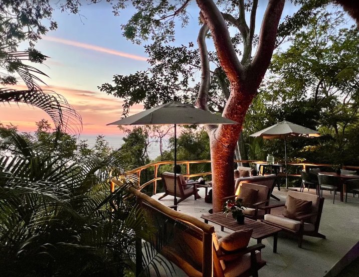 Open-air lounge with umbrellas and wicker chairs overlooking a sunset ocean view