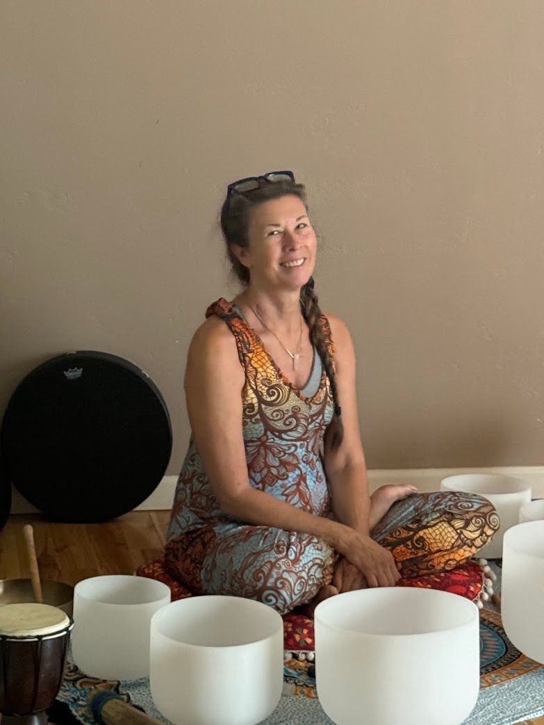 A woman is sitting on the floor surrounded by bowls and a drum.