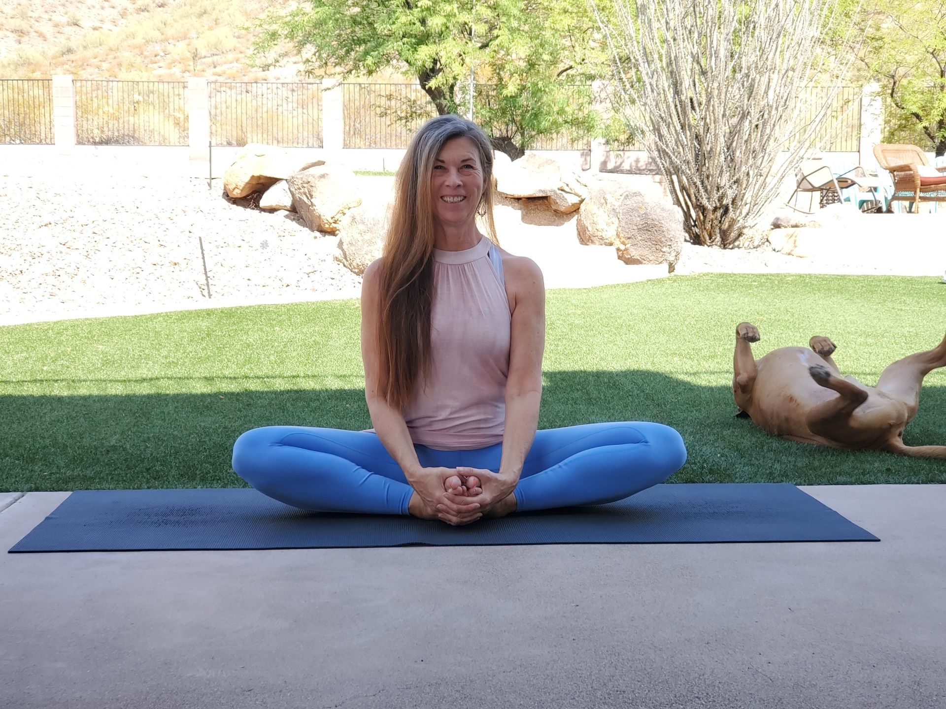 A woman is sitting on a yoga mat next to a dog.