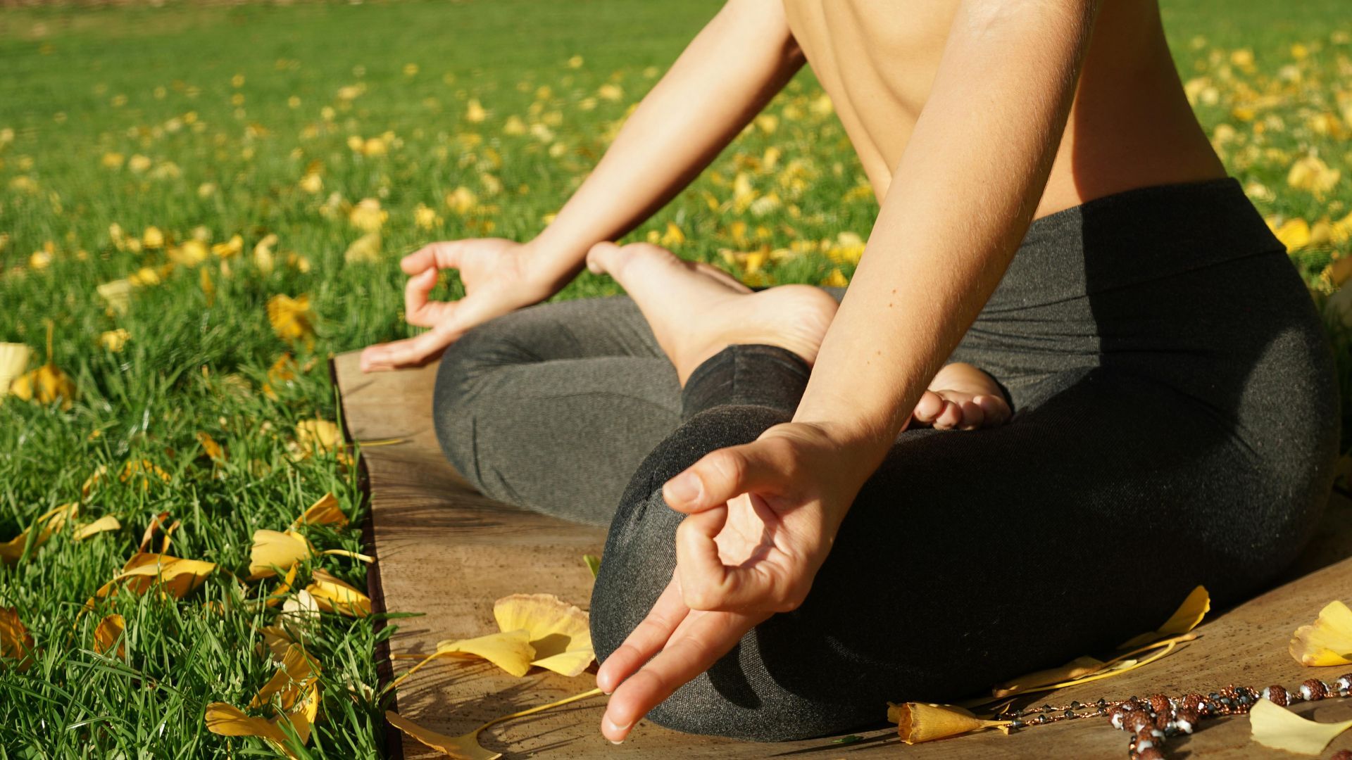 A woman is sitting in a lotus position on a yoga mat in a park.