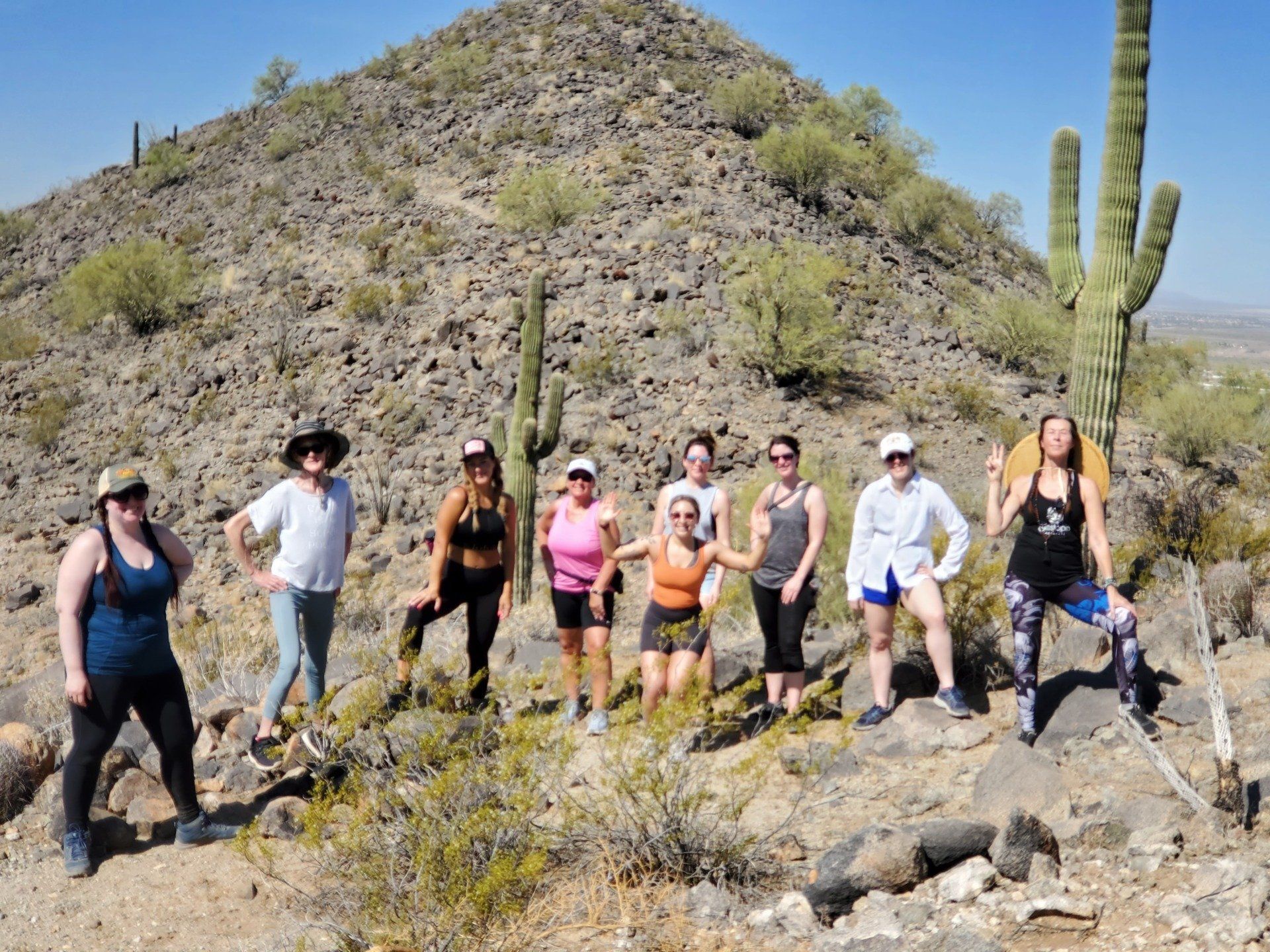 Group hiking through a rocky desert trail with tall cacti and a hill in the background