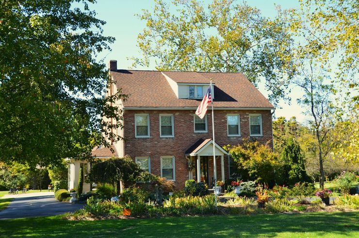 Brick suburban house with an American flag, front porch, and a landscaped yard in bright sunlight
