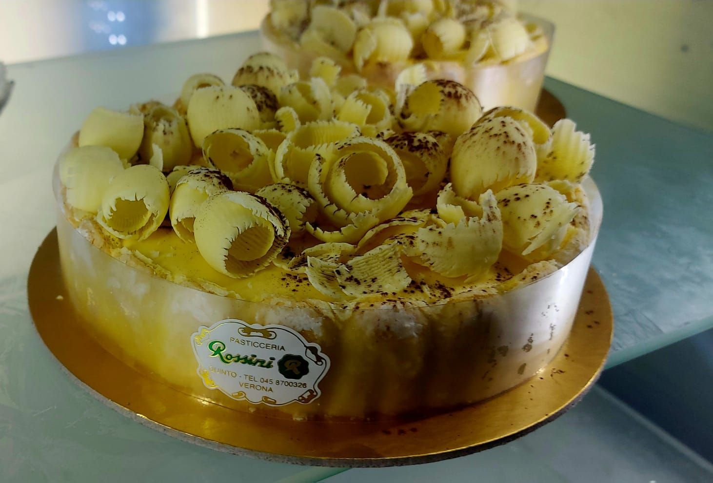 Torta con glassa gialla e riccioli di cioccolato bianco su un piatto dorato.