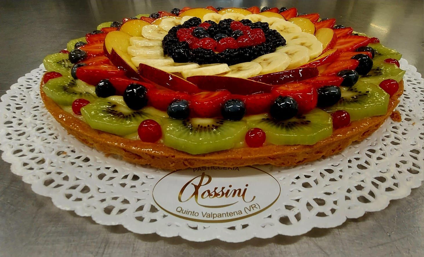 Crostata di frutta con kiwi, fragole, mirtilli, banane e pesche su un centrino di pizzo.