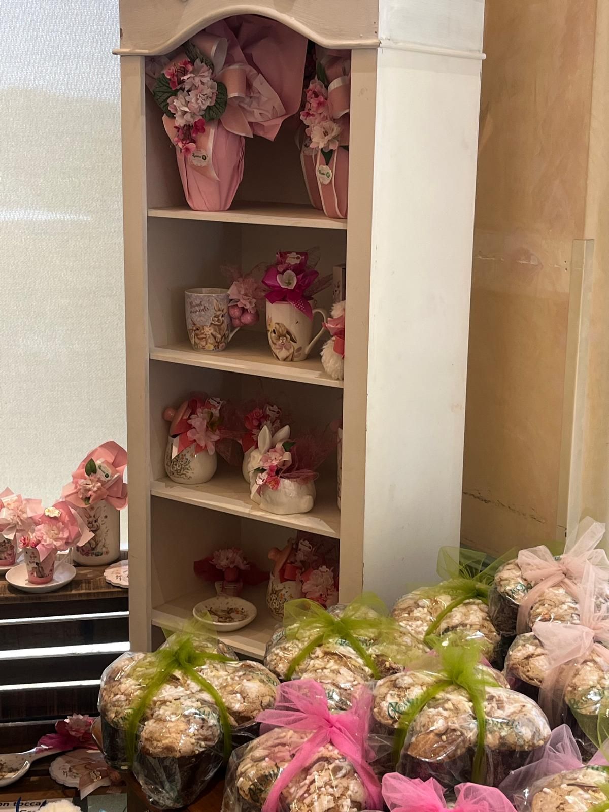 Una mensola bianca espone tazze da tè e vasi con composizioni floreali. In primo piano, dolci da forno confezionati.