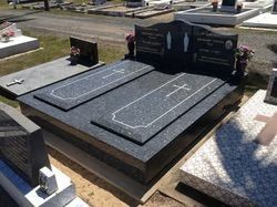 Black granite double headstone with two grave markers, cross symbols, and floral arrangements — Mackay Monumental Masons In Glenella, QLD