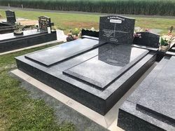 Dark granite headstone and flat grave markers in a cemetery — Mackay Monumental Masons In Glenella, QLD