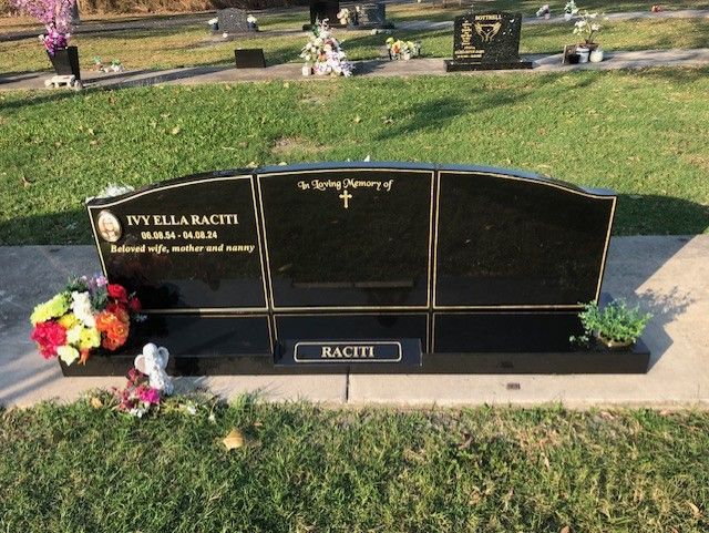 Polished black headstone with flowers in a cemetery.