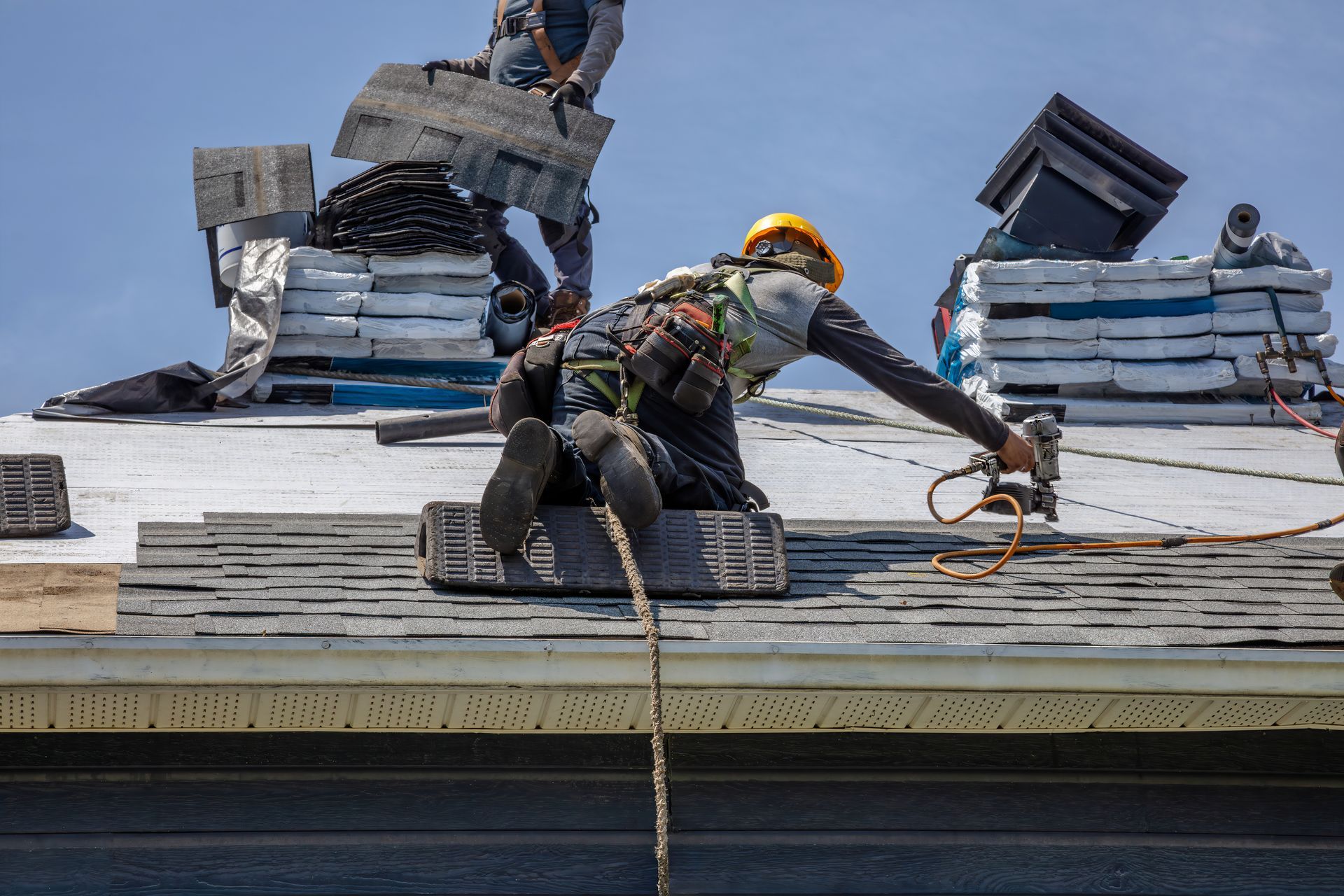 Roofing workers installing shingles on a sloped roof, using nail guns