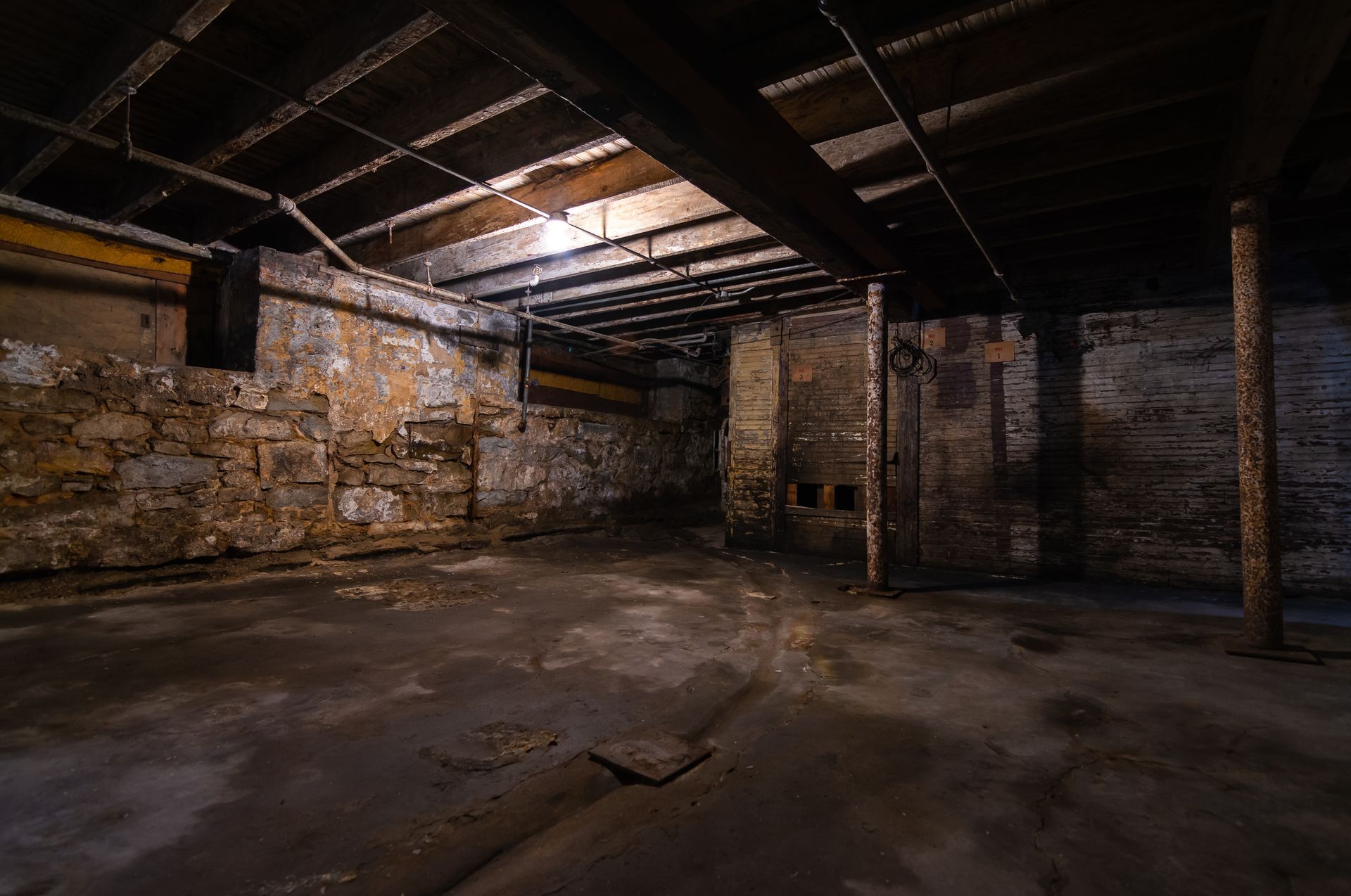 Dank basement with concrete floor, stone walls, and exposed beams.