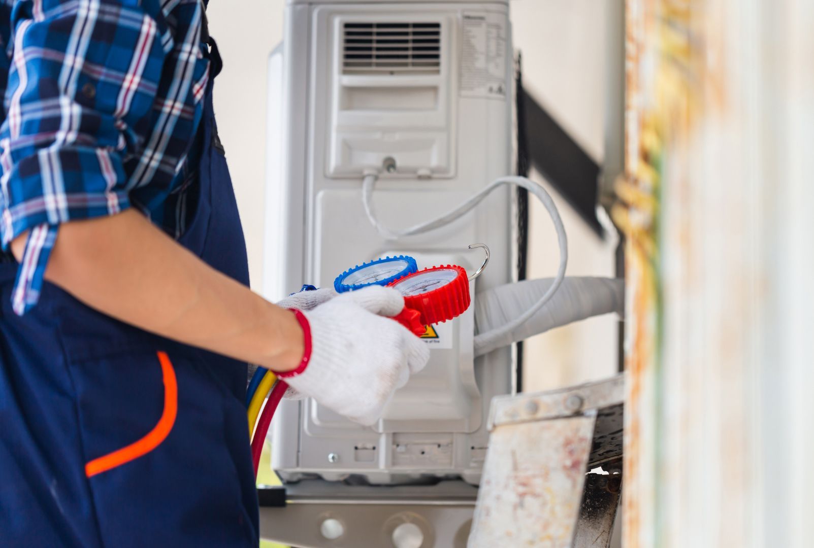 A man is working on an air conditioner with a manifold pressure gauge.