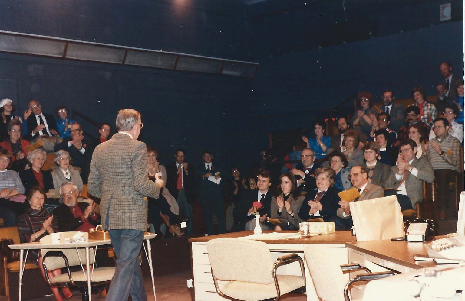 Opening night of the first show at 1501 New Hampshire Man speaking to a crowd in a dark auditorium. People clap, some are in suits.