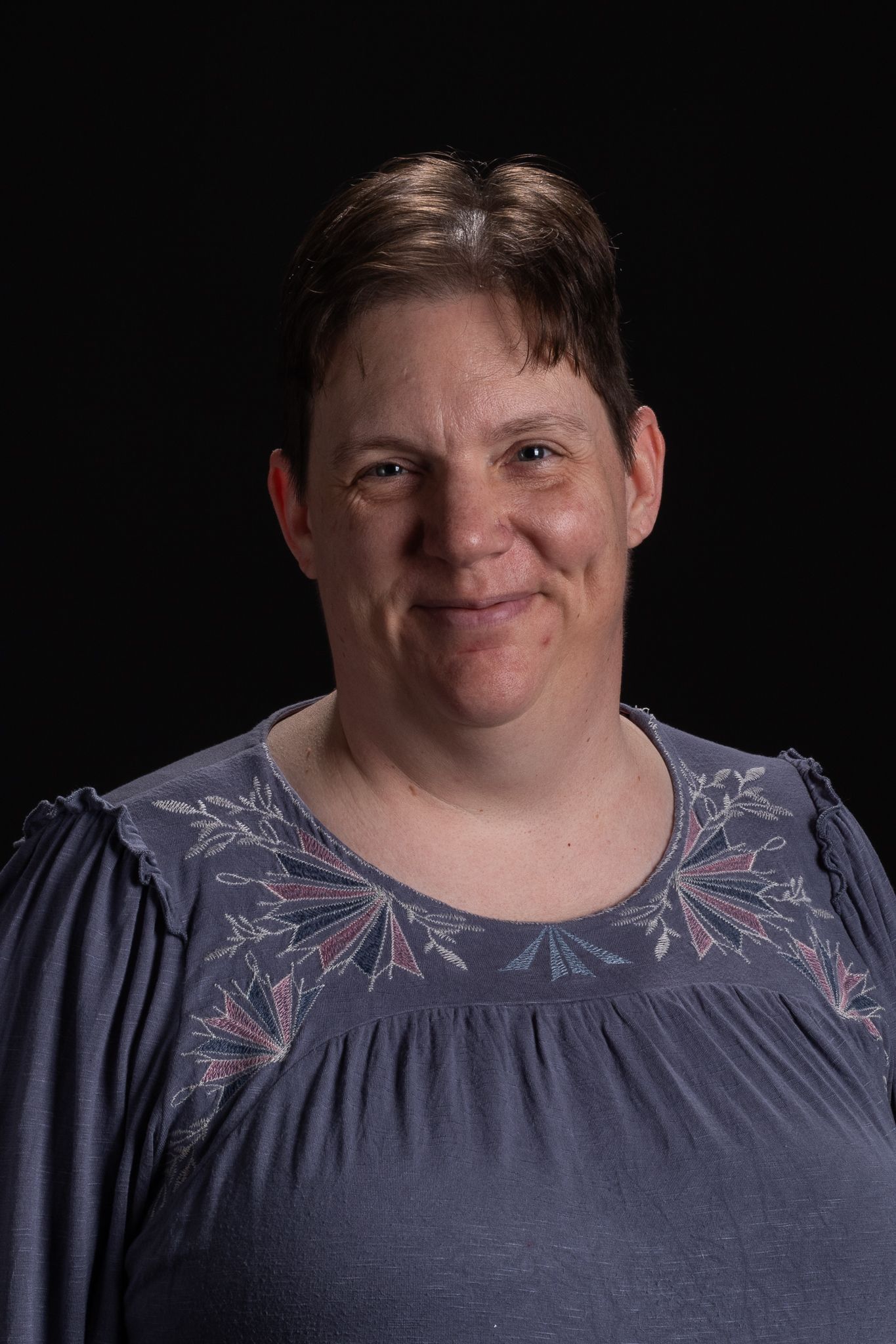 Smiling person in a blue patterned top against a dark background