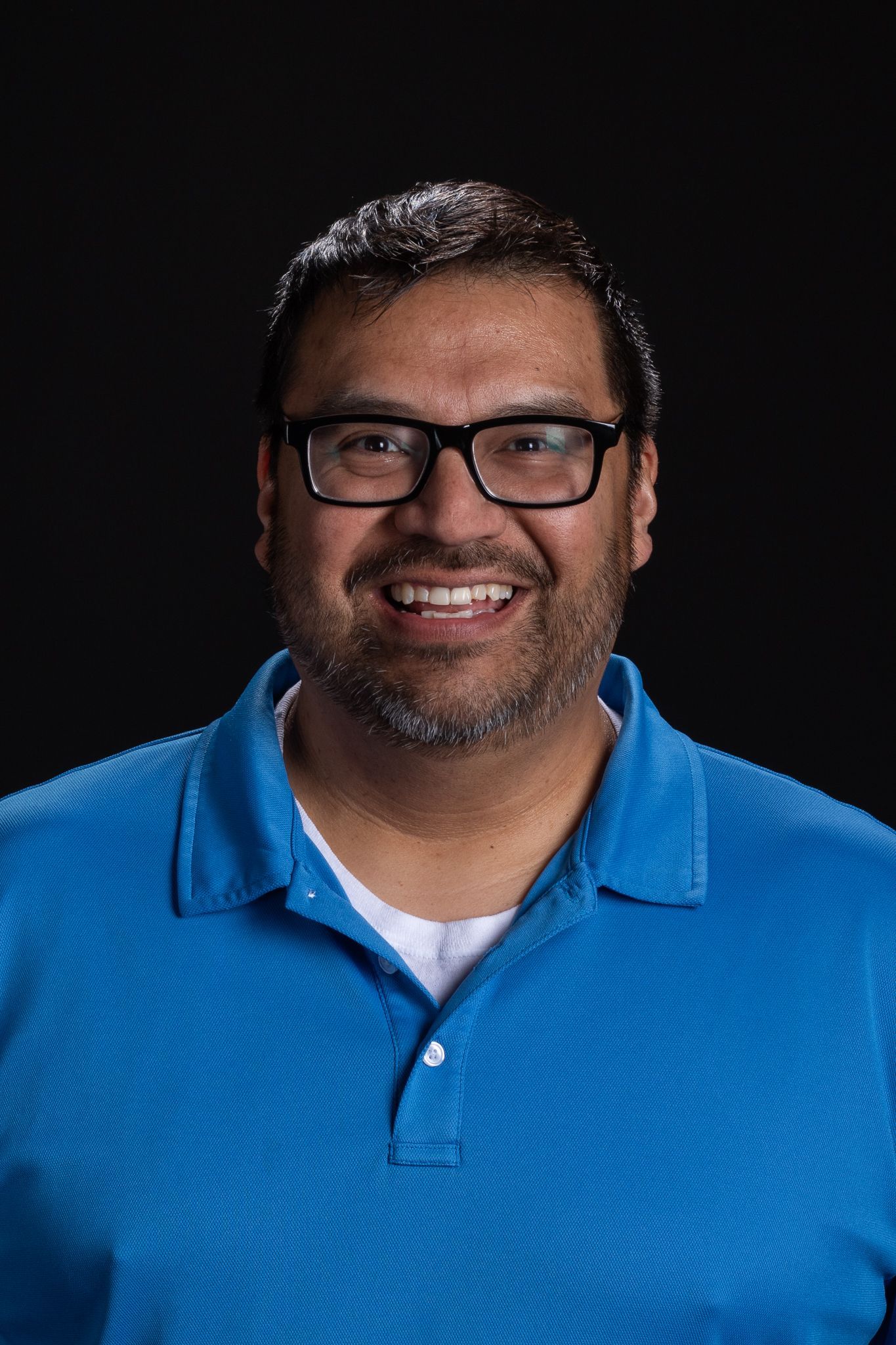 Smiling person in black glasses and a blue polo shirt against a dark background