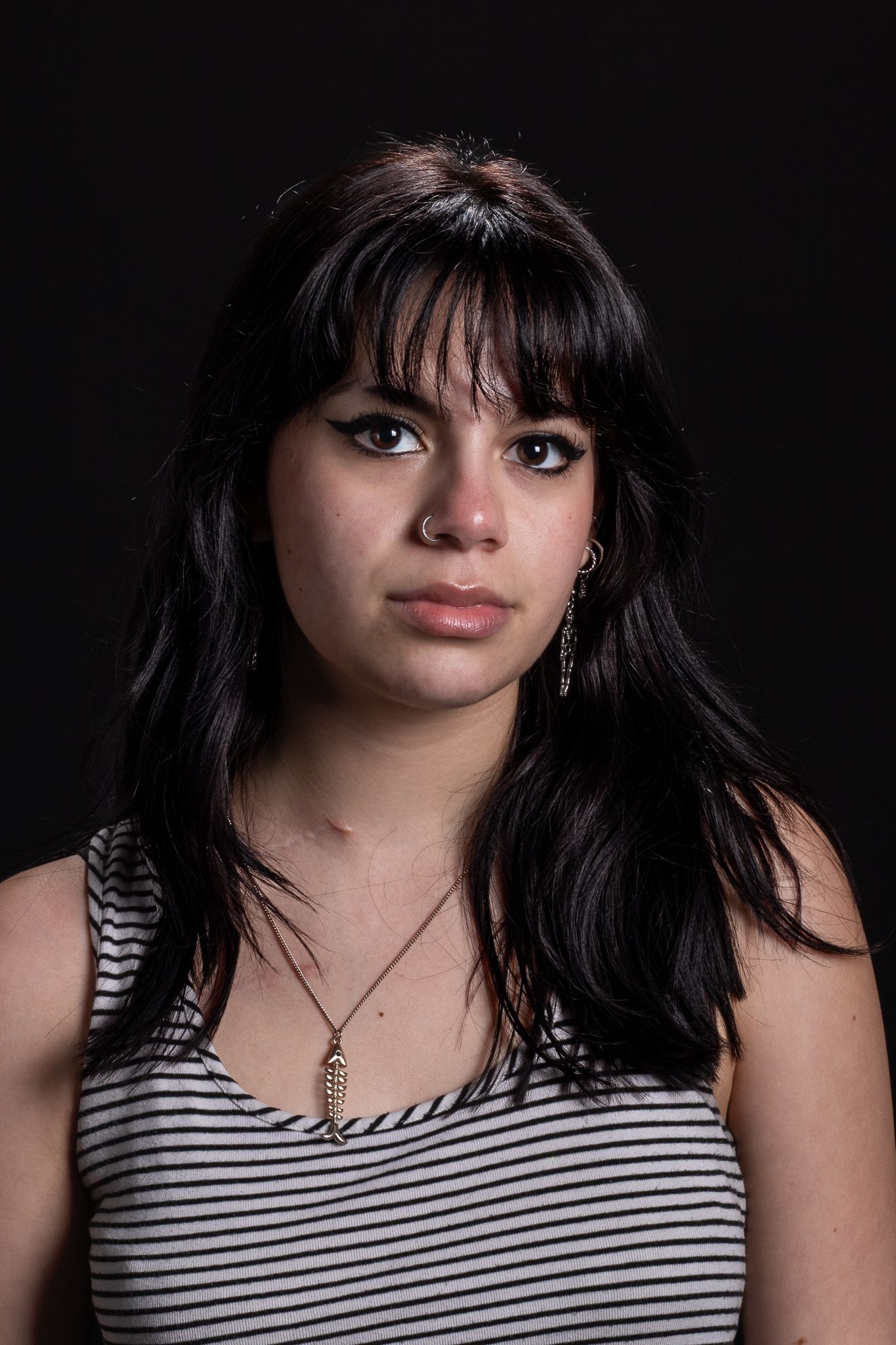 Portrait of a woman with dark hair and bangs, wearing a striped top against a dark background