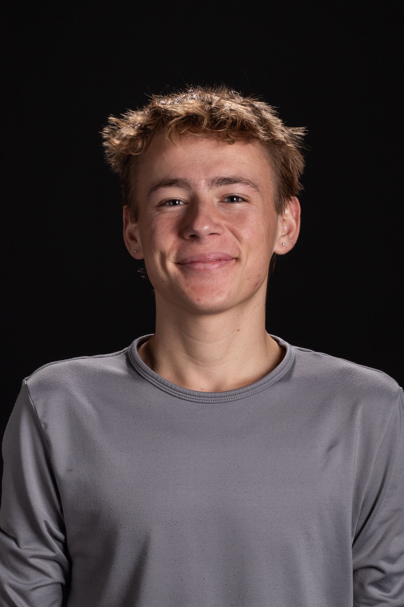 Portrait of a smiling person in a gray shirt against a black background