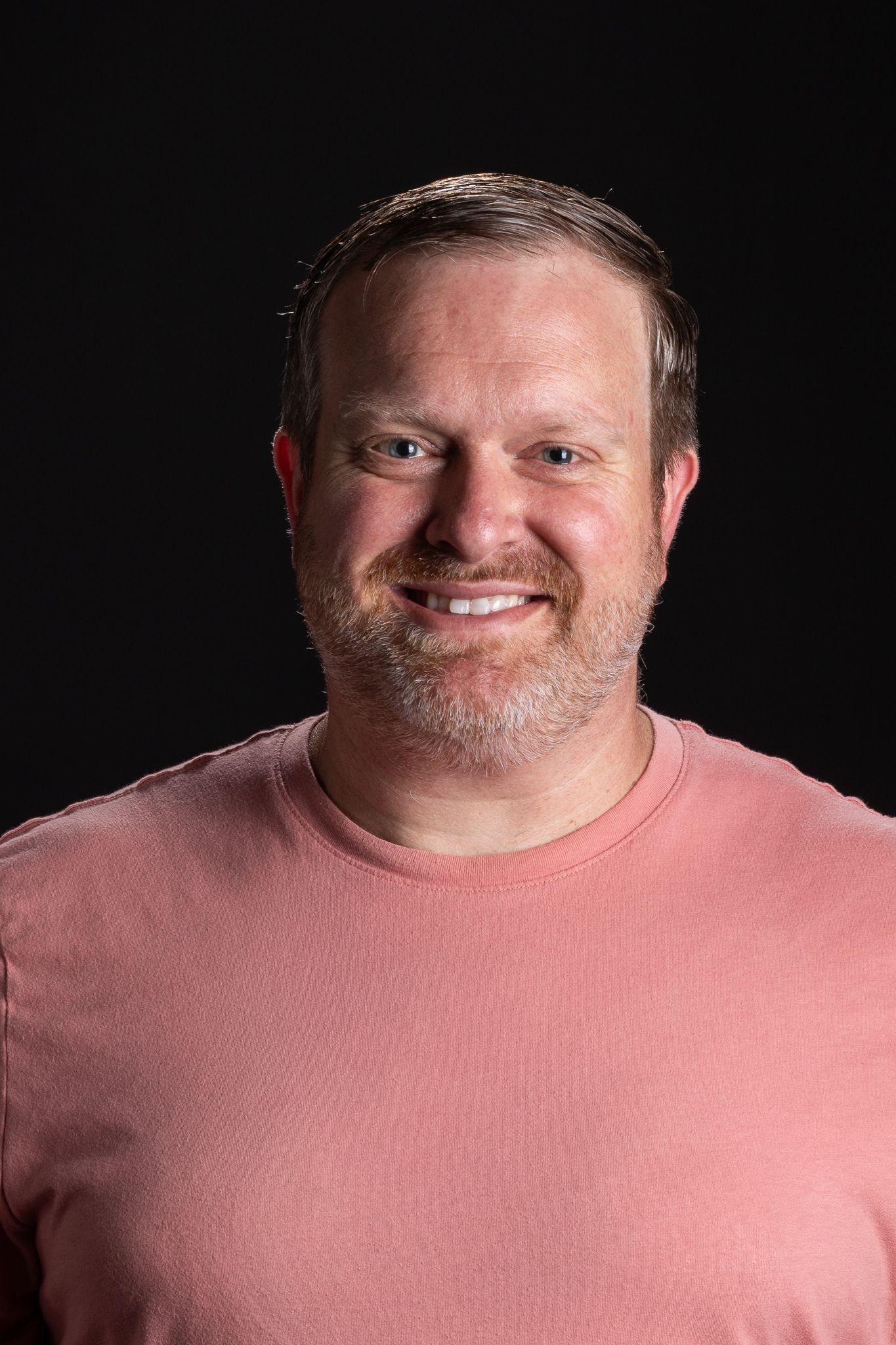 Smiling man in a pink shirt against a dark background
