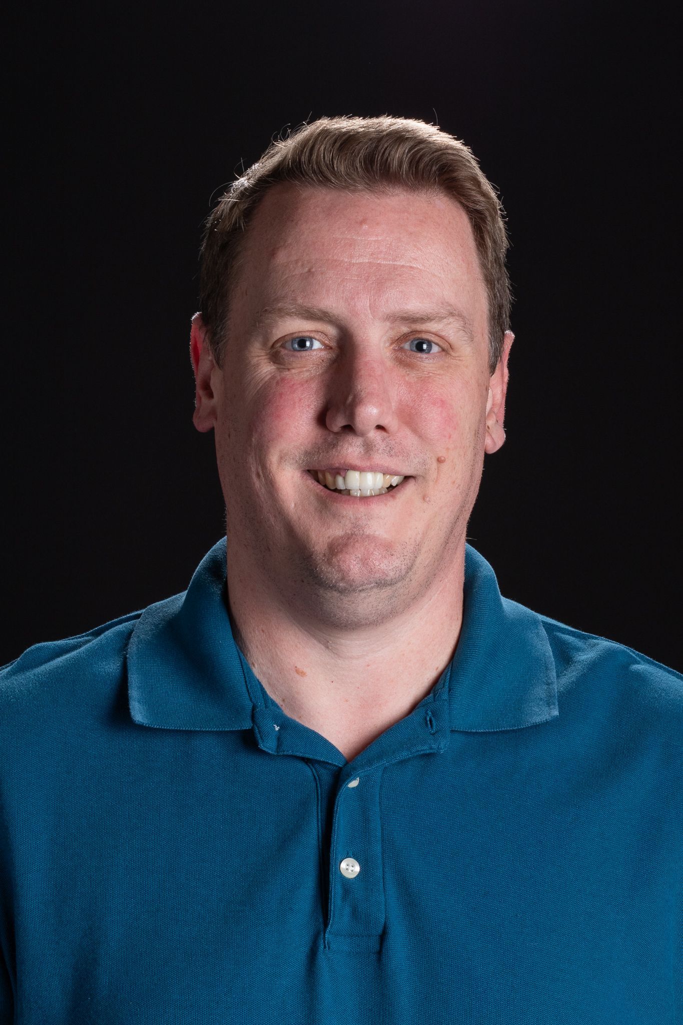 Smiling person in a blue polo shirt against a dark background