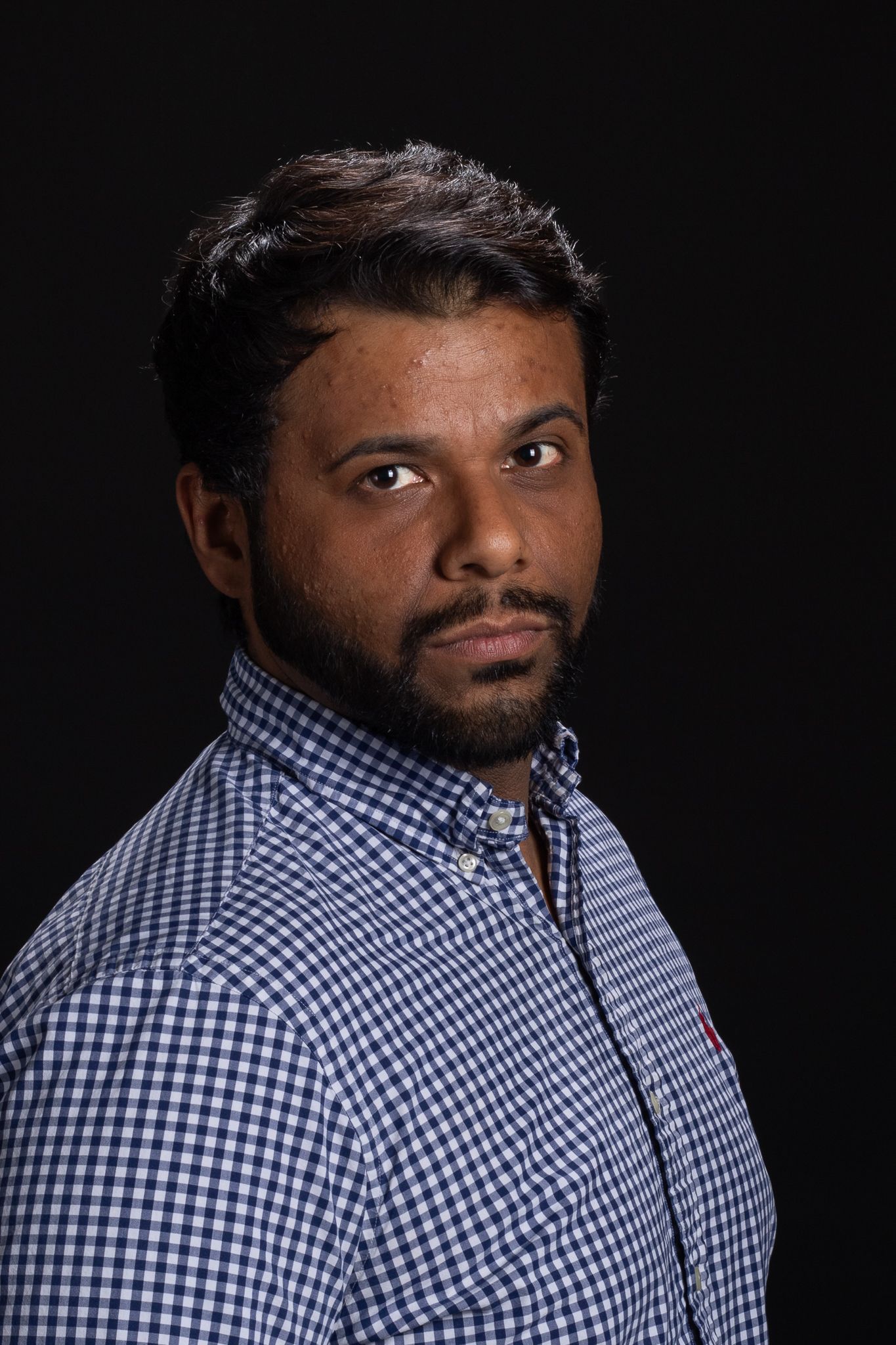 Portrait of a person in a blue checkered shirt against a dark background, looking at the camera