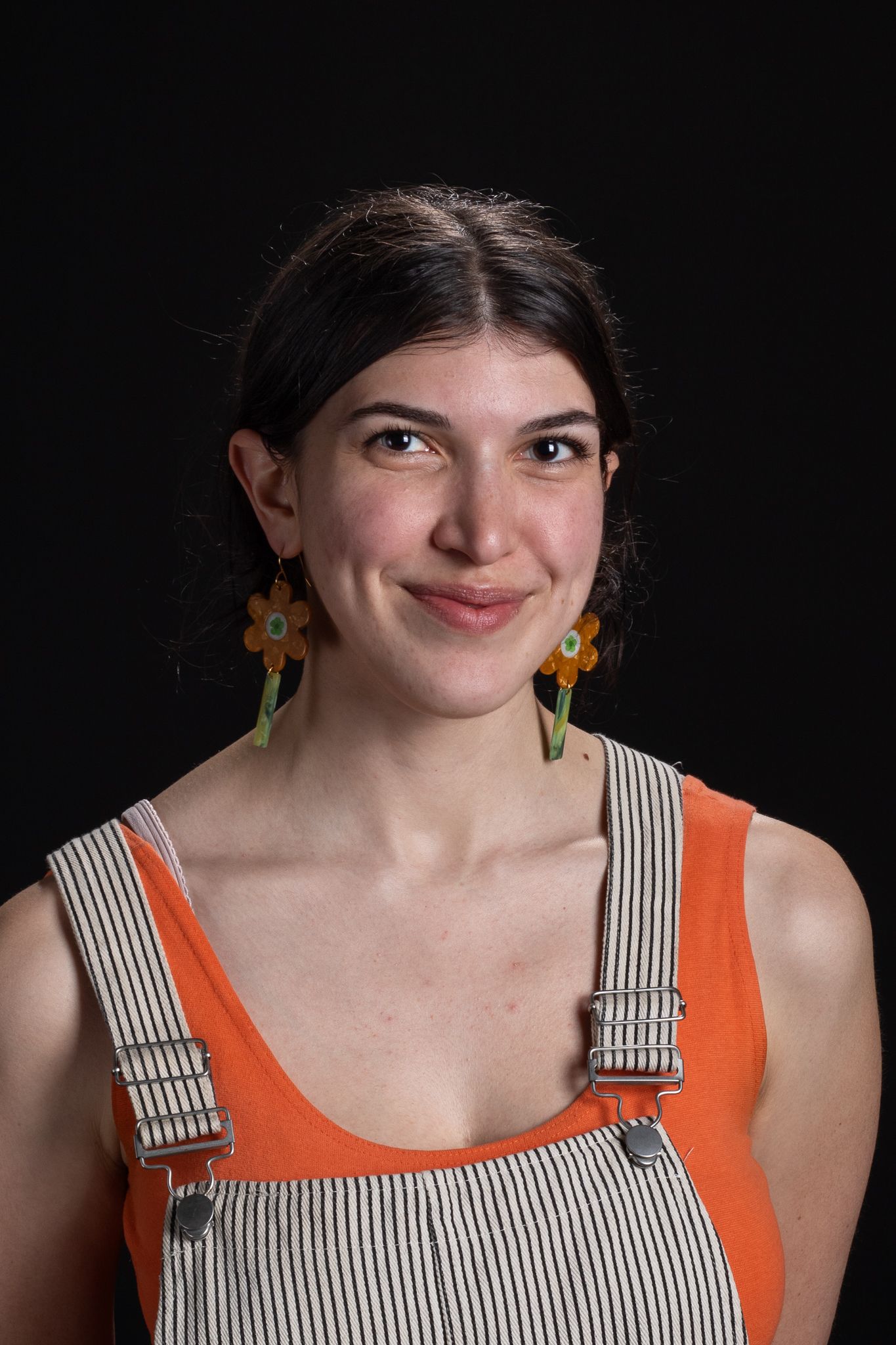 Portrait of a smiling person in an orange top with checkered overalls against a black background