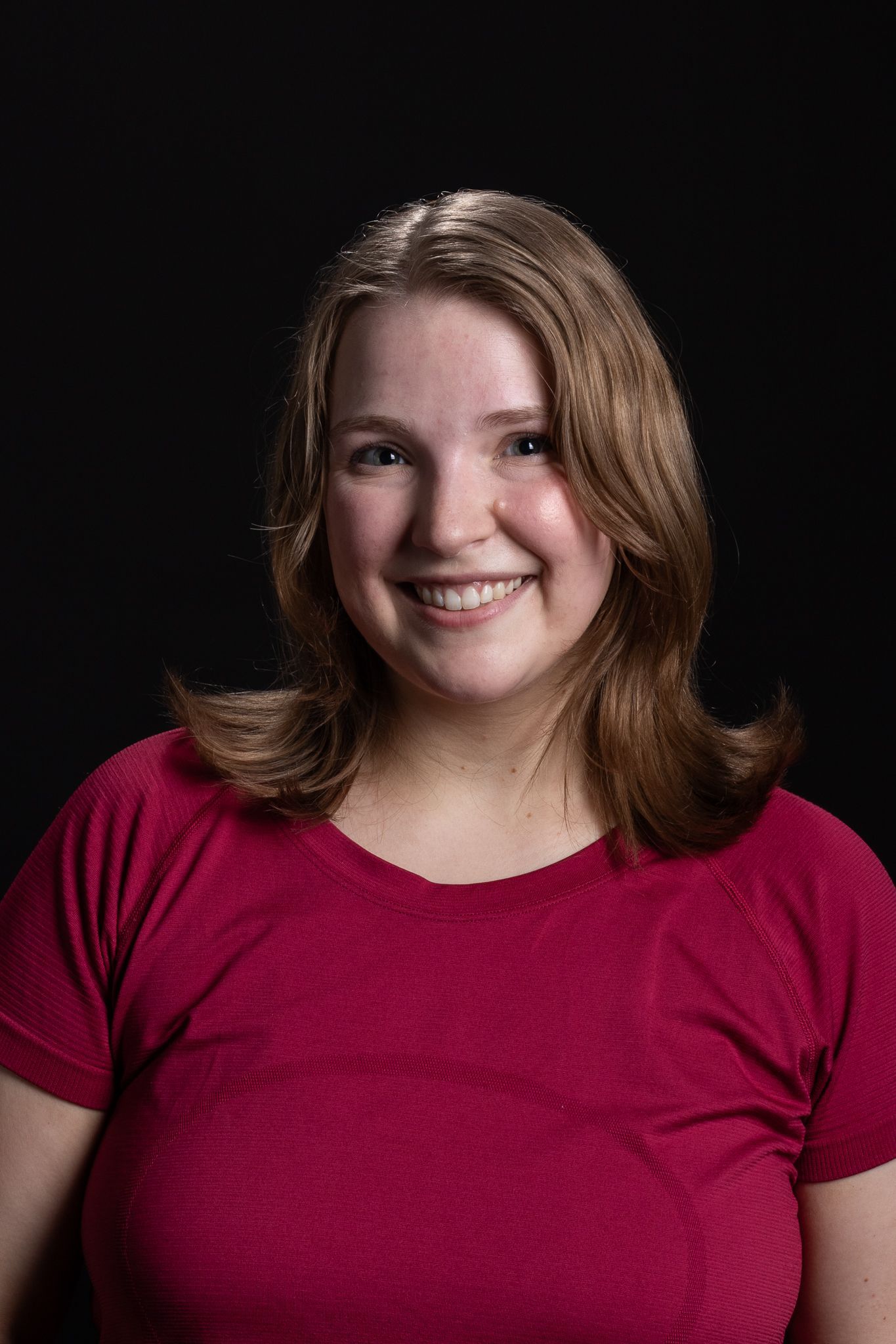 Smiling person in a red shirt against a dark background