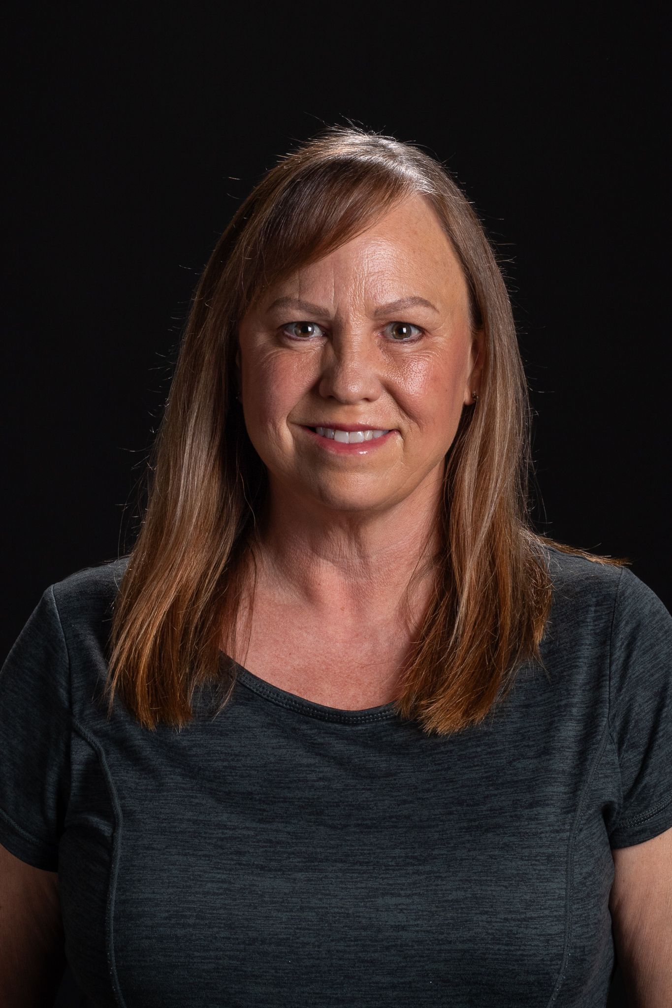 Portrait of a smiling woman with long brown hair against a black background