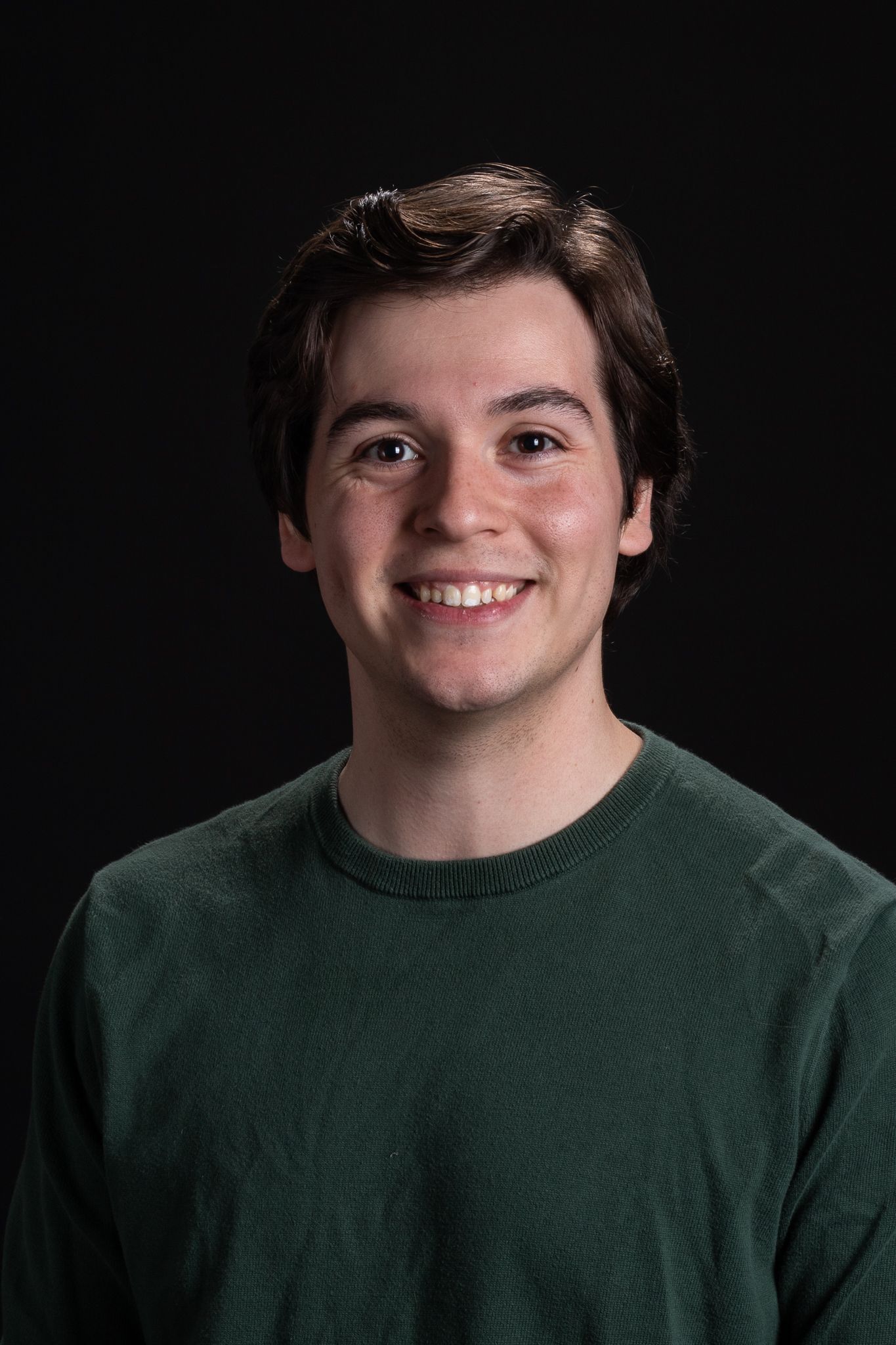 Smiling person in a dark green sweater against a black background