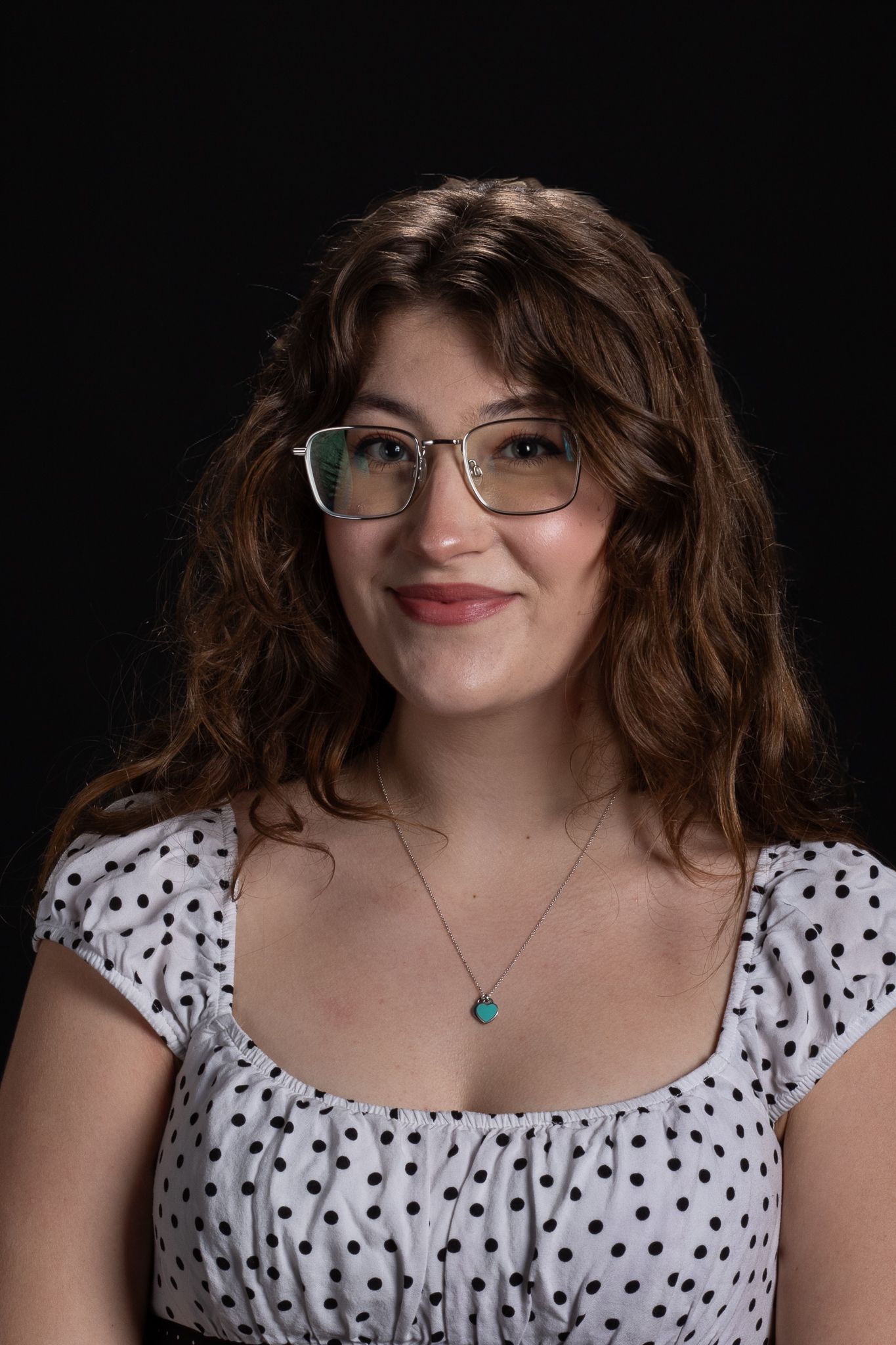 Portrait of a smiling woman with glasses in a white polka-dot top against a dark background