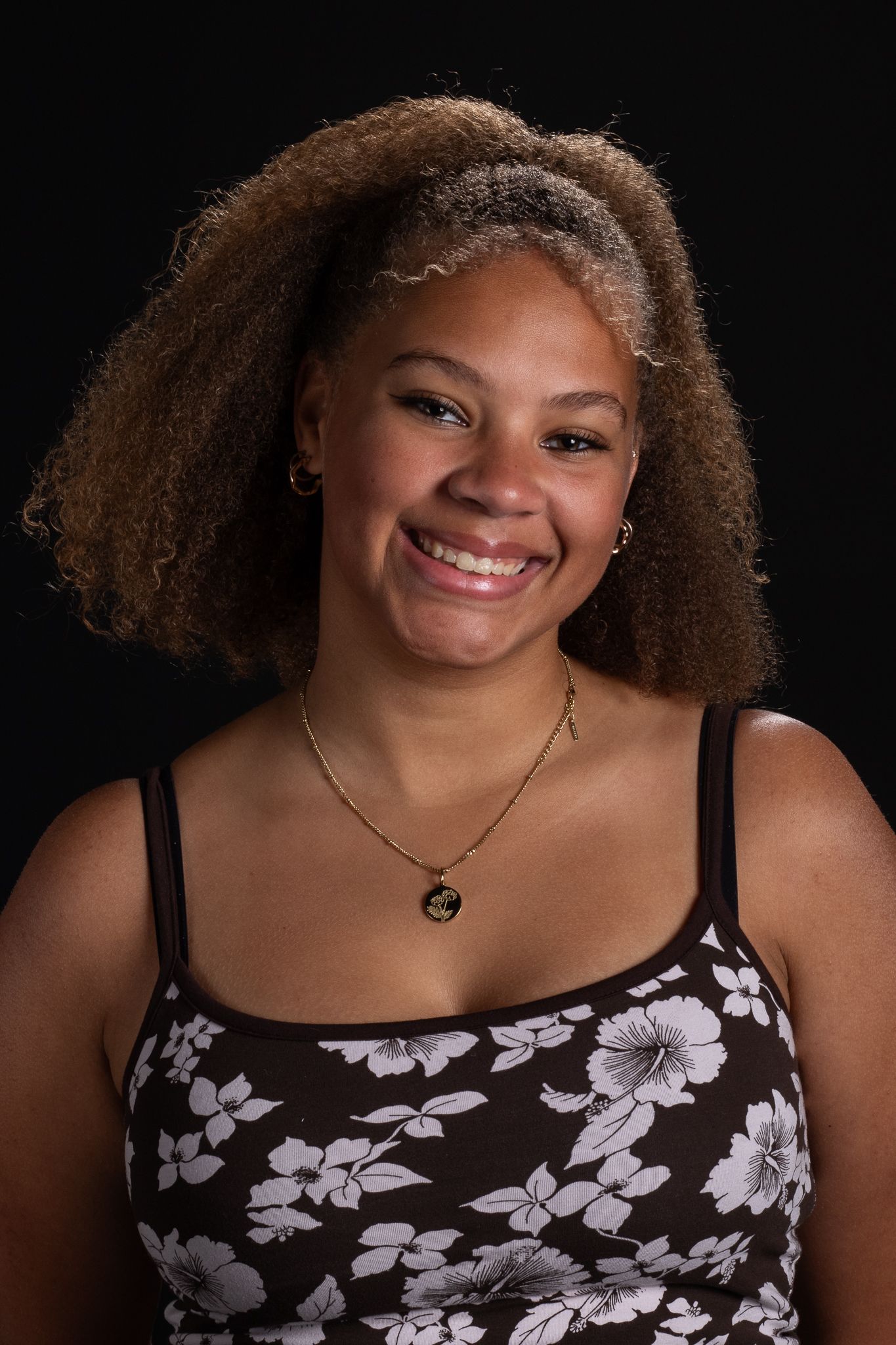 Smiling person with curly hair wearing a black floral top against a dark background