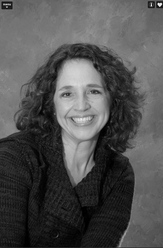 Smiling woman with curly hair in a dark sweater against a plain gray background