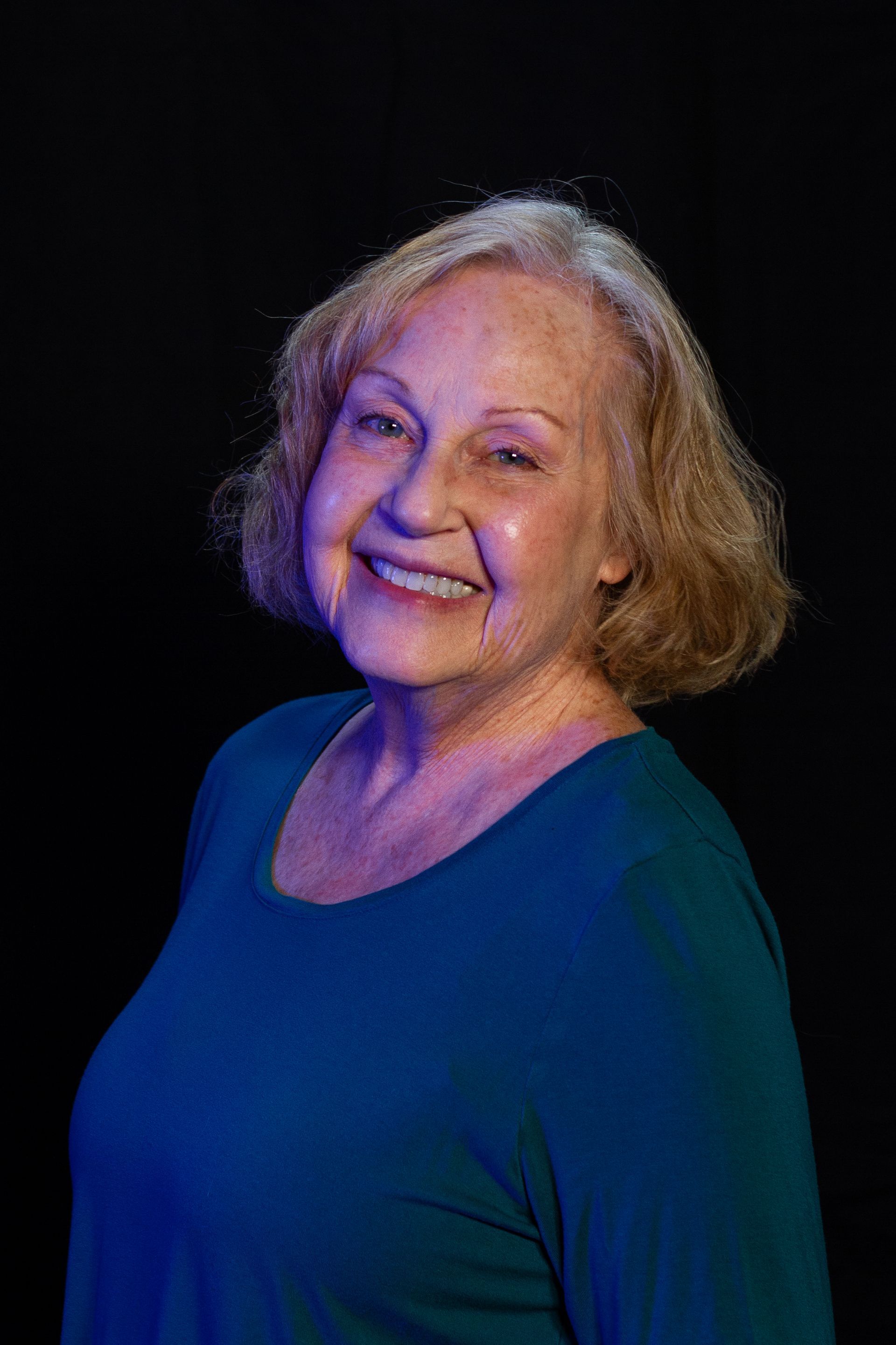 Smiling older woman in teal shirt against a black background.