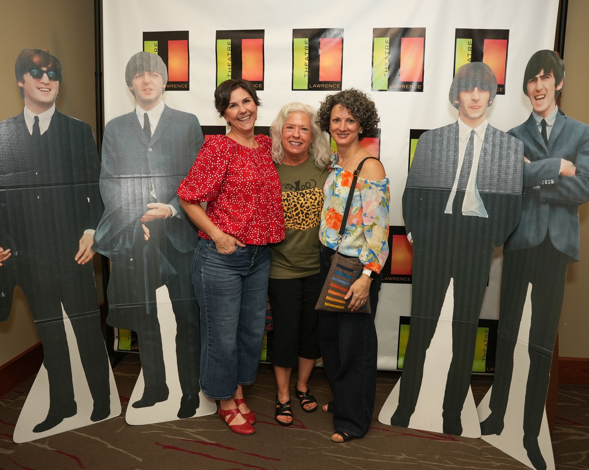 Three women pose with cardboard cutouts of The Beatles.