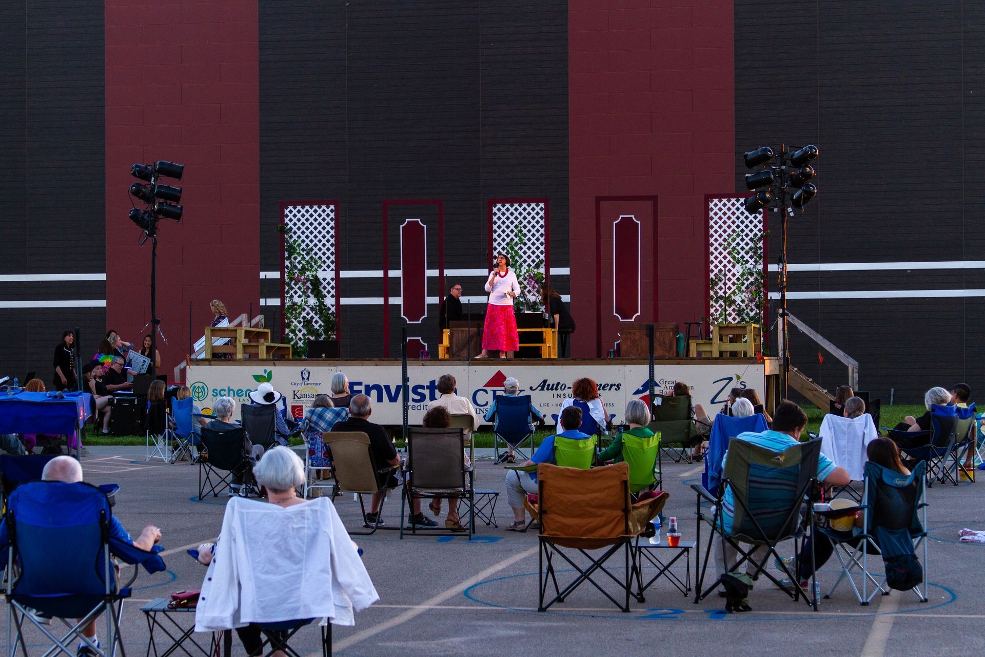 Outdoor stage, built during pandemic Outdoor stage with performer, audience in chairs. Dark red and black backdrop, evening.