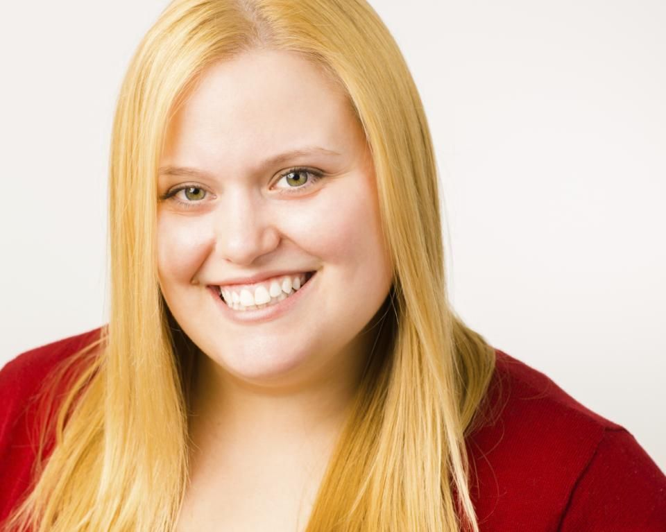 Blonde woman with a wide smile wearing a red top, against a white backdrop.