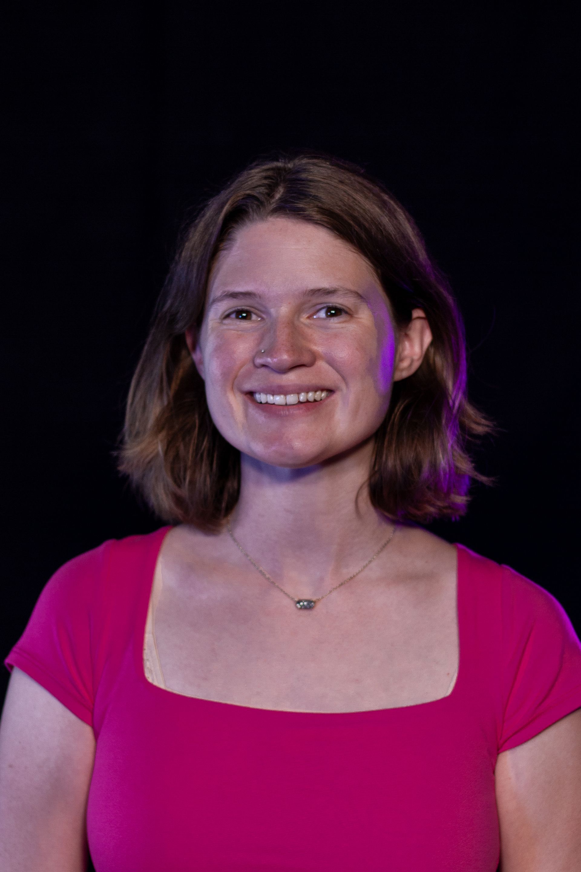 Woman in a pink top smiling, with a black background.