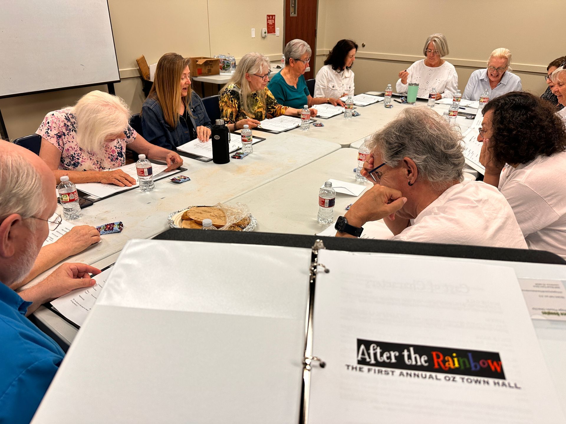 People seated around a long conference table in a meeting room, reviewing papers and notebooks